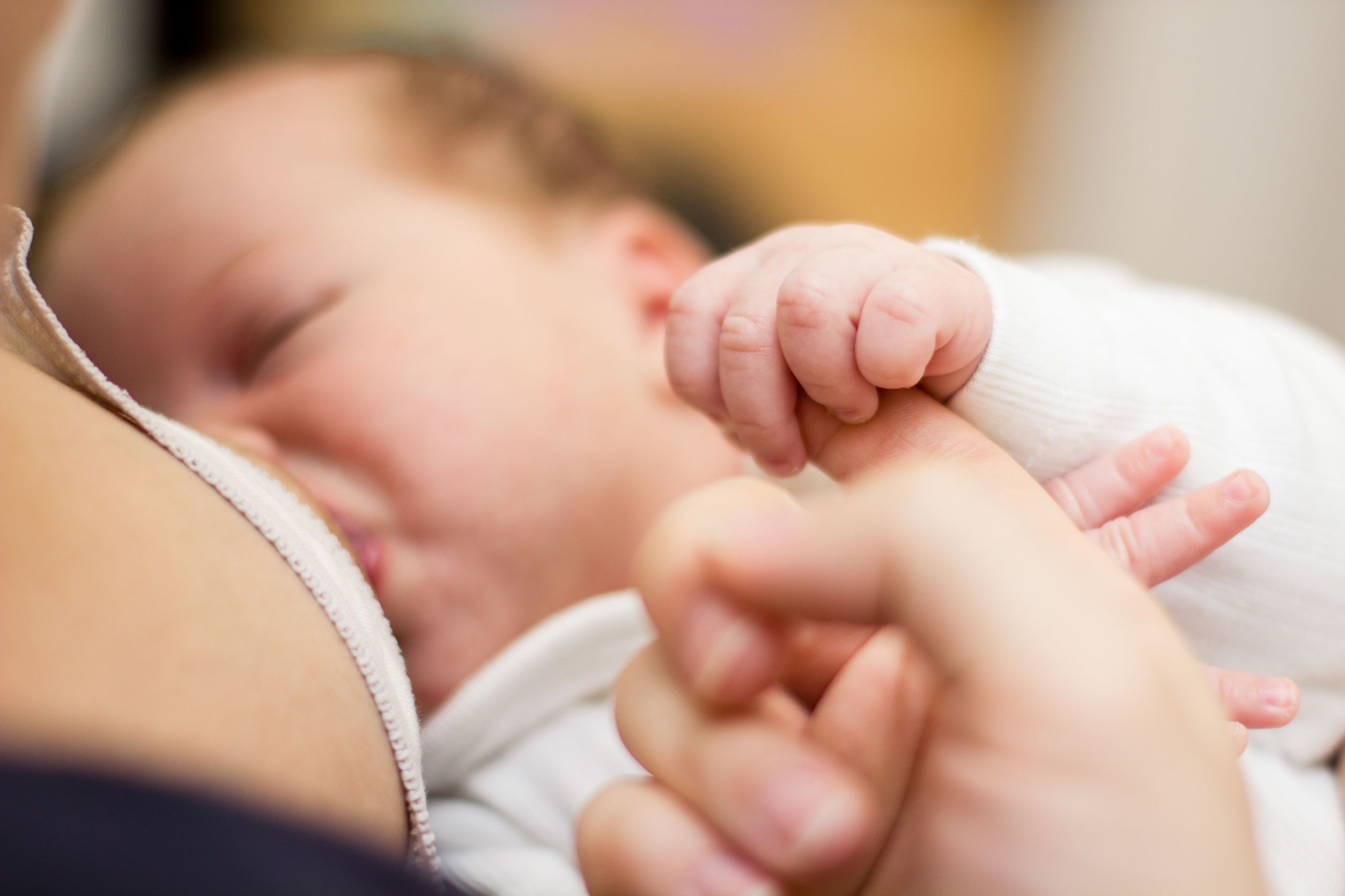 Newborn baby holding mother finger and breastfeeding