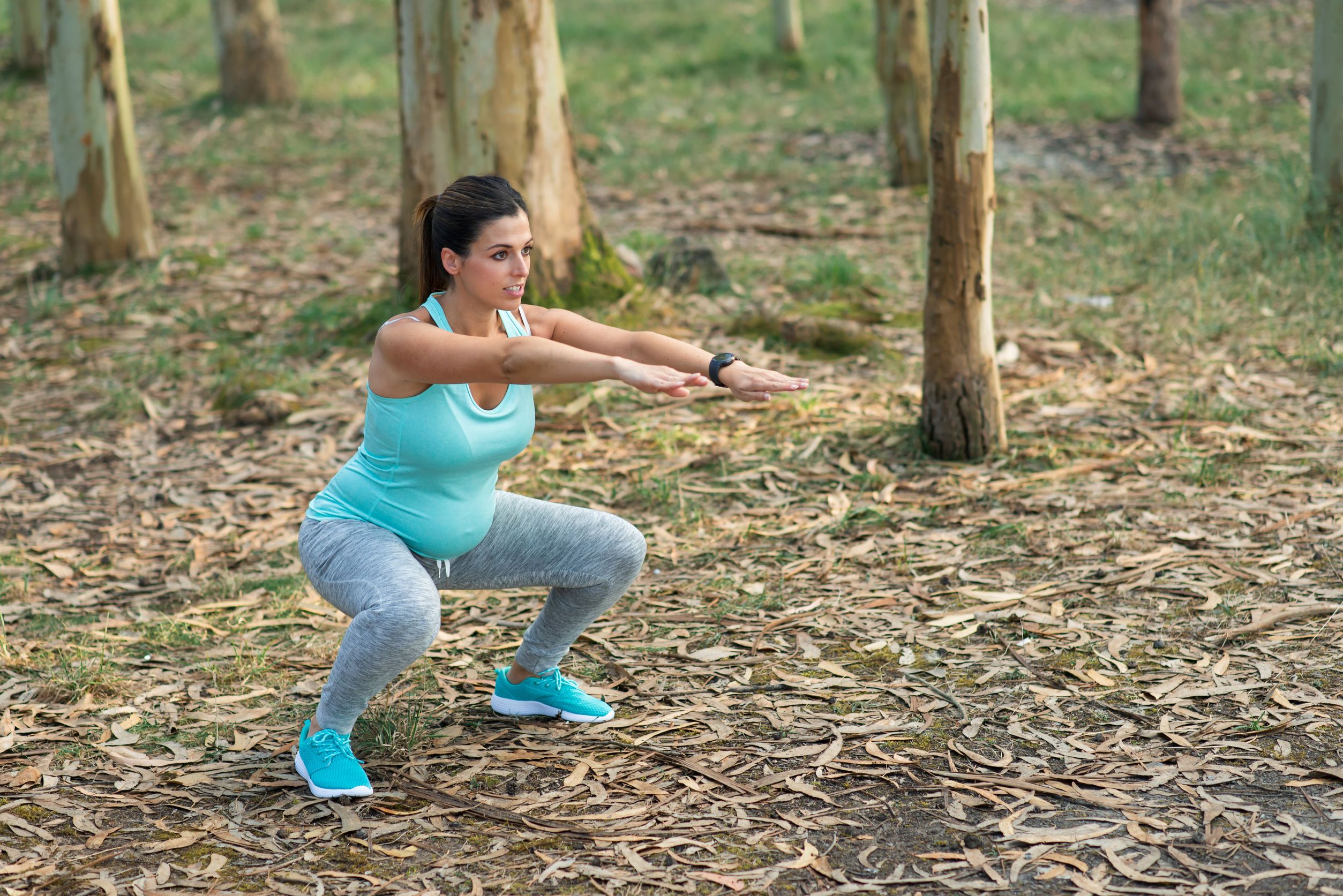 Pregnant fitness woman doing squats outdoor